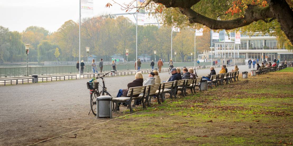 Menschen sitzen auf Bänken am Nordufer der Maschsee und blicken auf das Gewässer.